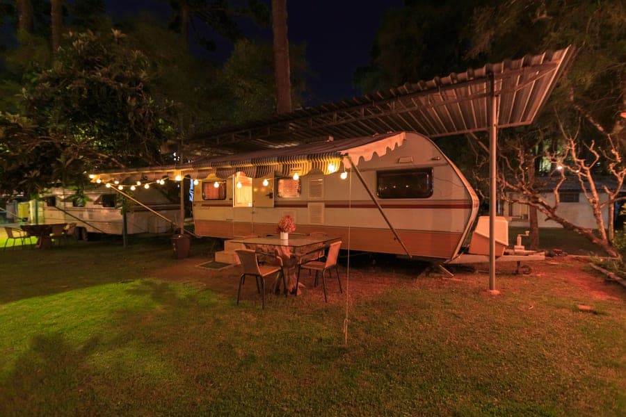 A retro camper trailer strung with warm lights at a campsite in the evening