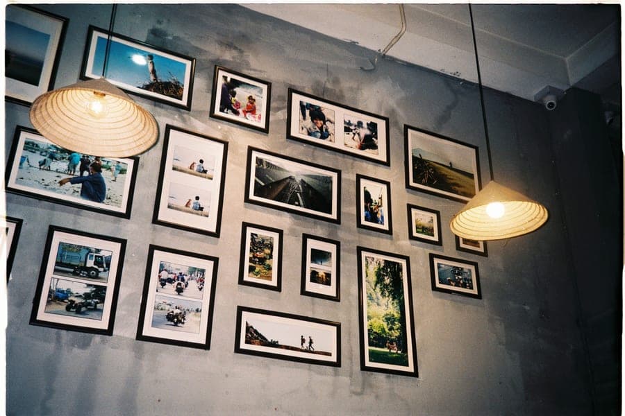 A gallery wall of framed photographs on a gray wall under pendant lights