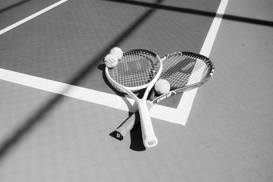 Two tennis rackets and tennis balls lying on a court, in black and white