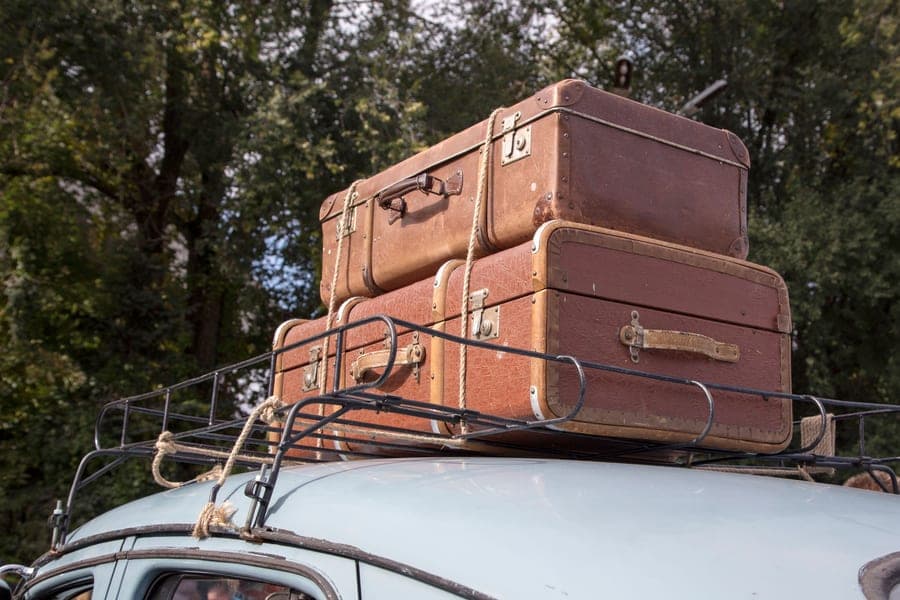 Vintage leather suitcases strapped to the roof rack of a classic car