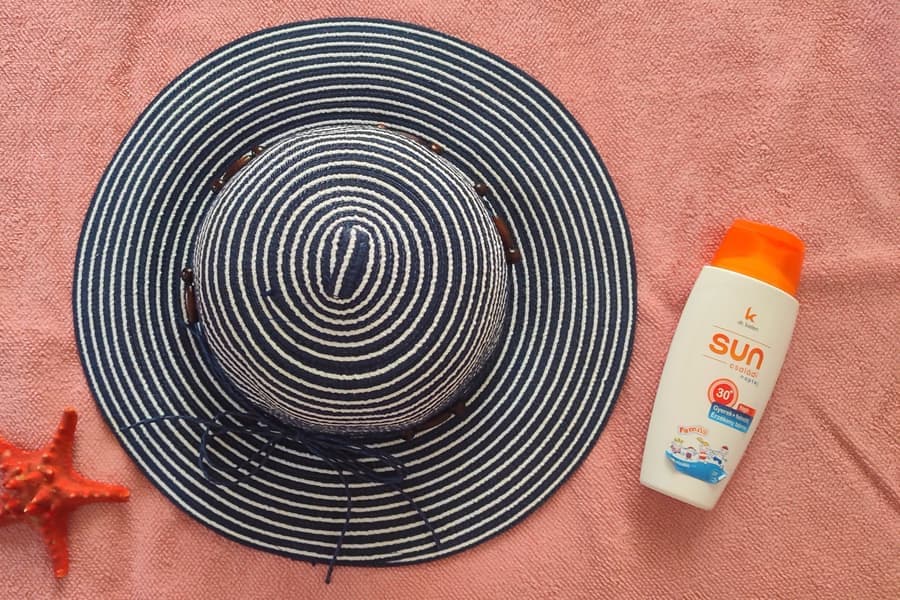 A striped sun hat, a bottle of sunscreen and a starfish on a pink towel