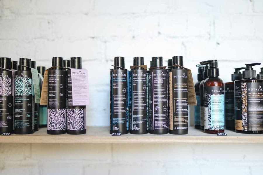 A row of hair care bottles lined up on a wooden shelf
