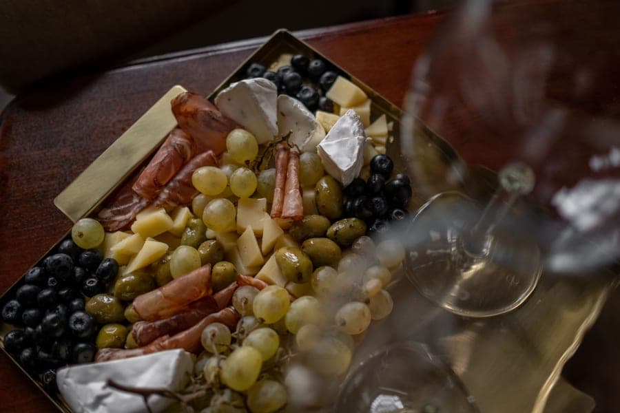 A cheese and charcuterie board with olives, grapes and a wine glass on a tray